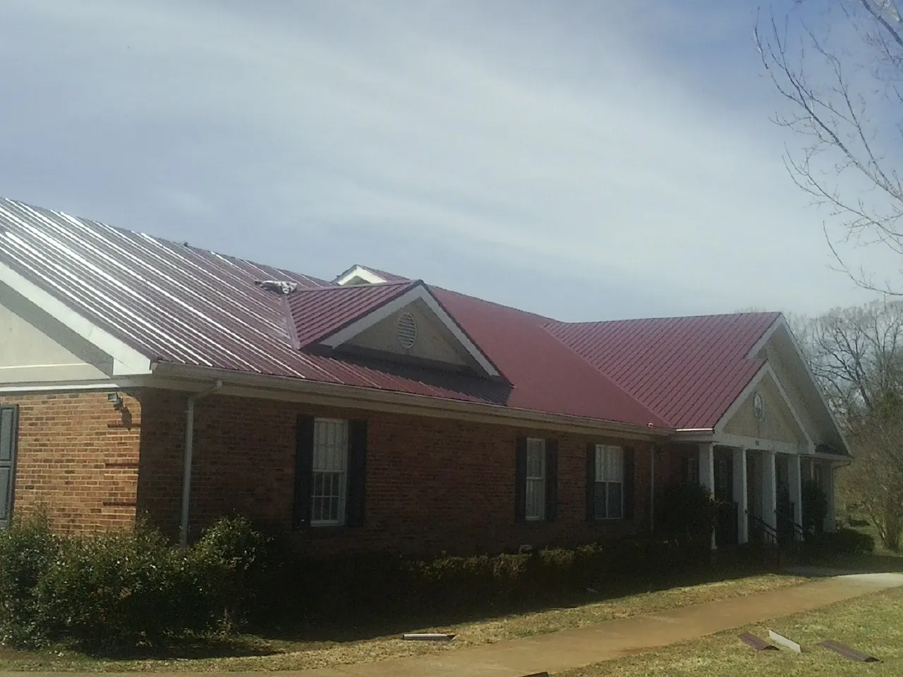 Red metal roof with gabled entries on a long brick building, from a Hail Damage Roof Repair job in Lenni