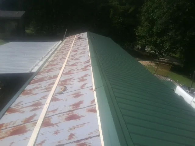 Old rusted panels beside newly installed green metal roofing — Wind Damage Roof Repair by Roofing Brothers in Lenni