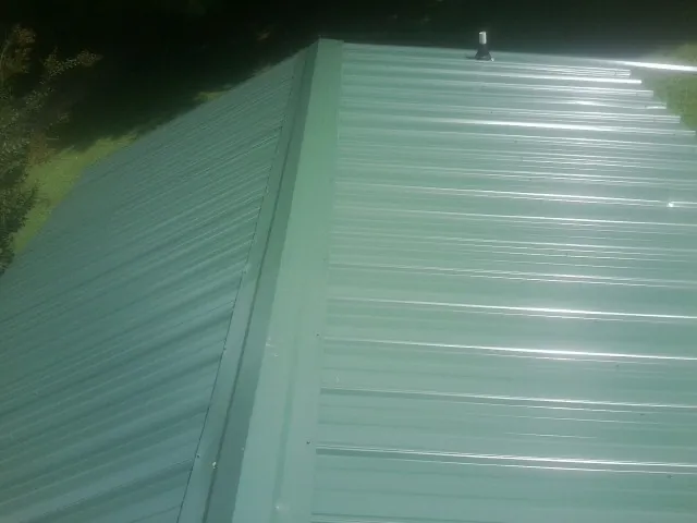 New green metal panels meeting at the ridge of a roof — Flat Roof Repair work by our crew in Lenni