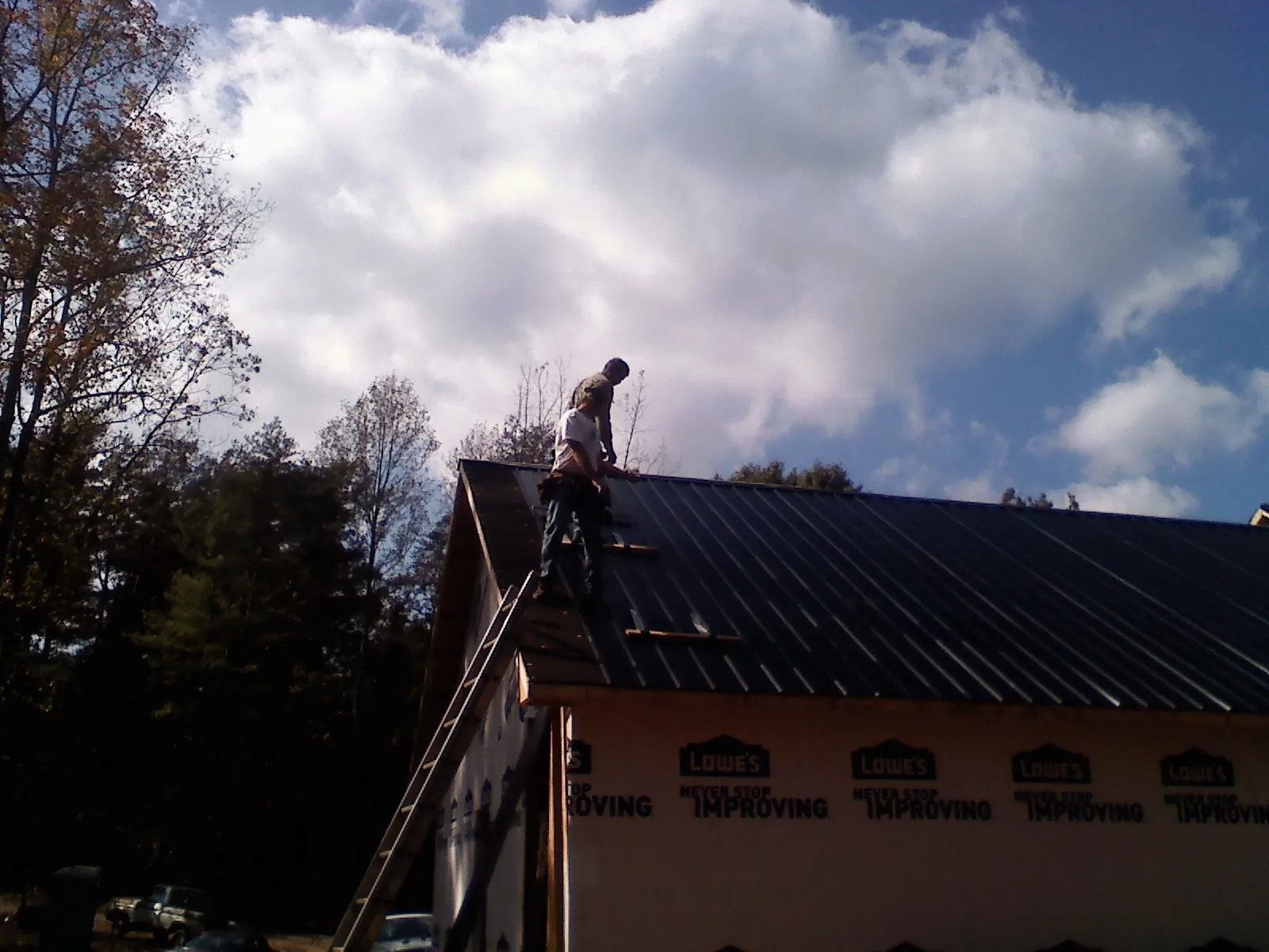 Roofer fastening dark metal panels high against a cloudy sky, from a Roof Inspection job in Lenni