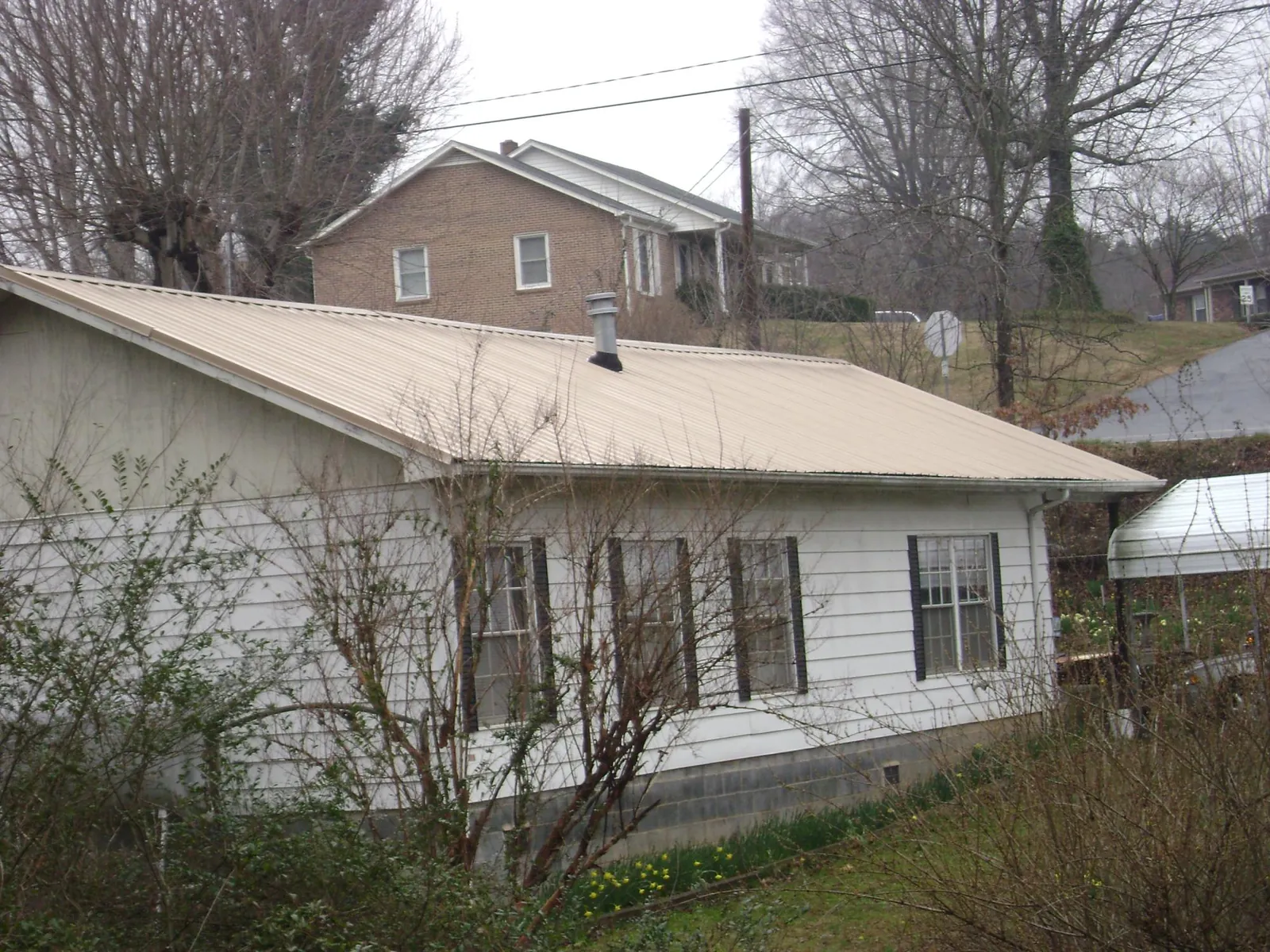 Tan metal roof on a white sided house set into a hillside — Commercial Roofing by Roofing Brothers in Lenni