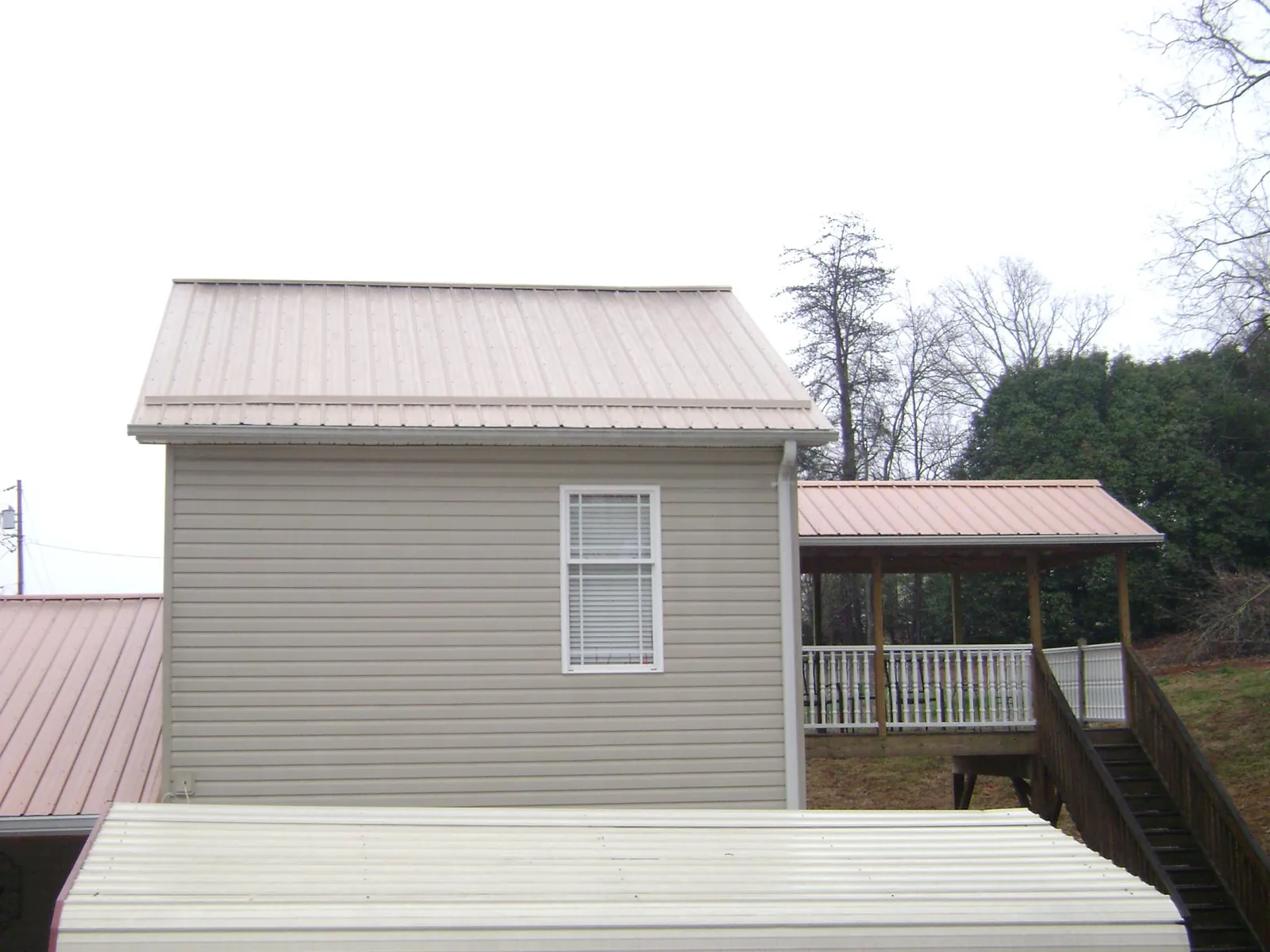 Tan metal roofs on a two story addition and attached porch, from a Roof Replacement job in Lenni